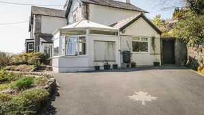 A two-story house with a conservatory, a garage, and a driveway with a maple leaf marking. - Yewbarrow Cottage (Grange-over-Sands)