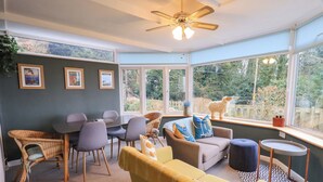A cozy room with a dining area, a sofa, and a window with a view of trees. - Yewbarrow Cottage (Grange-over-Sands)