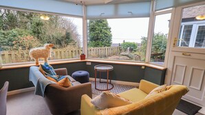 A cozy corner with a brown sofa, a yellow sofa, and a blue ottoman. There is a small round table and a decorative sheep sculpture on the windowsill. - Yewbarrow Cottage (Grange-over-Sands)