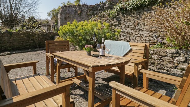 A wooden outdoor seating area with a table and chairs, a bottle of wine, and a wine glass. - Yewbarrow Cottage (Grange-over-Sands)