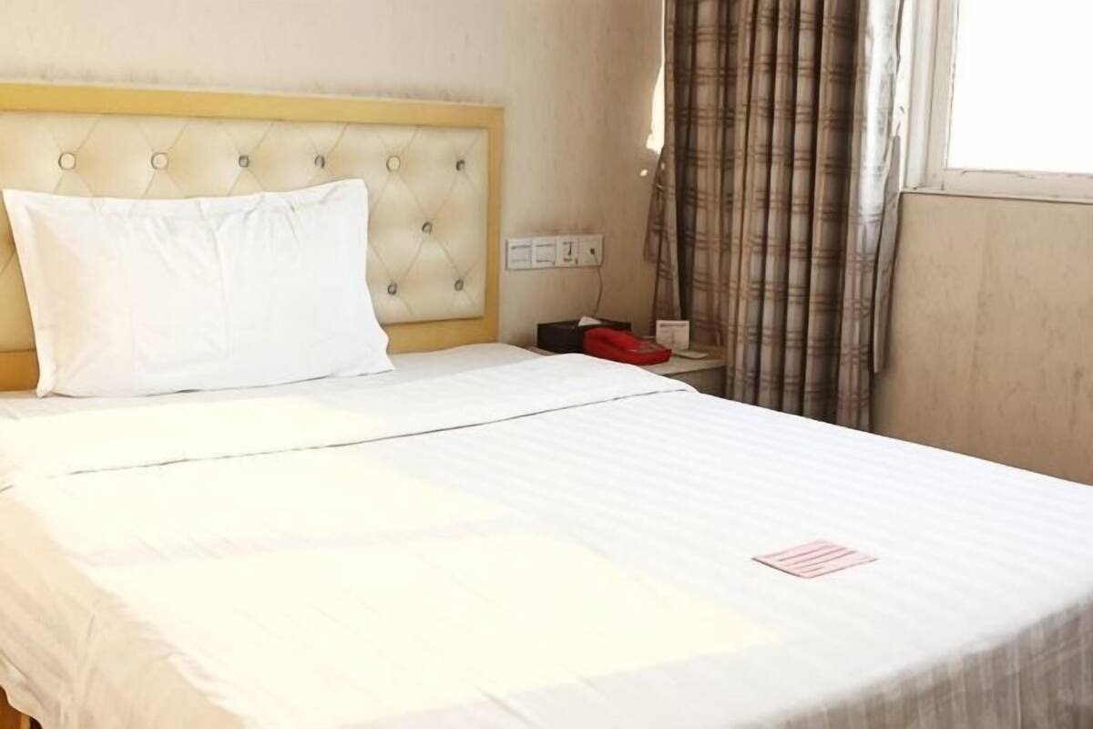 A hotel room with a bed, a headboard, a nightstand, a telephone, and a window with curtains.