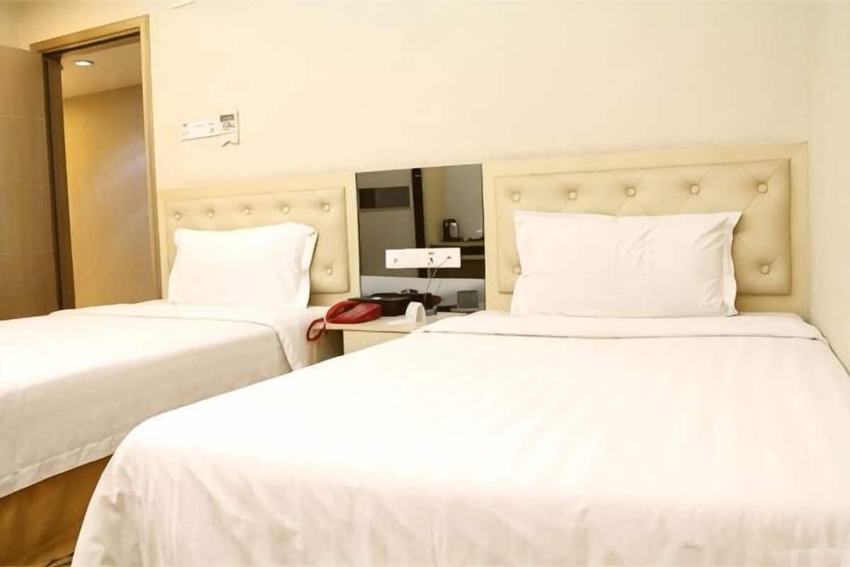 A hotel room with two beds, a bedside table with a red telephone, and a mirror.
