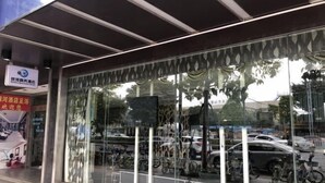 A hotel entrance with a large glass window reflecting parked bicycles and cars. - Xiaolan Yinhe Business Hotel (Zhongshan)