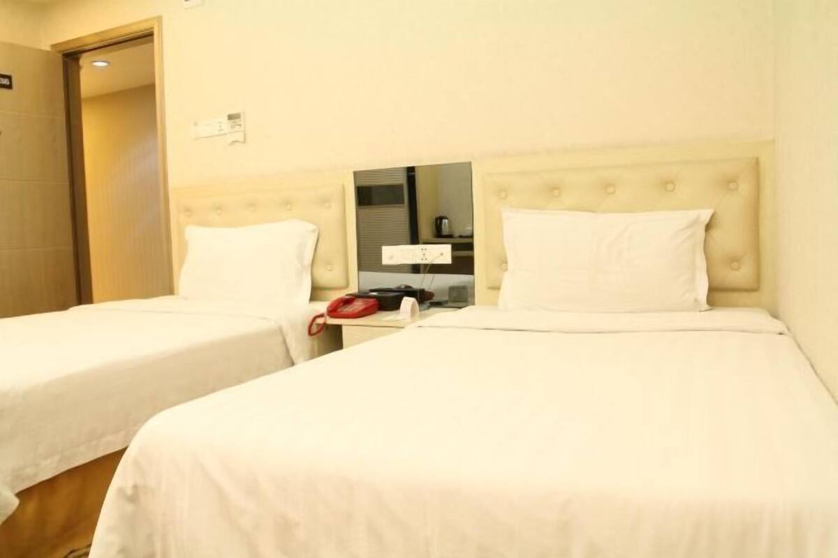 A hotel room with two beds, a bedside table with a telephone, and a mirror.