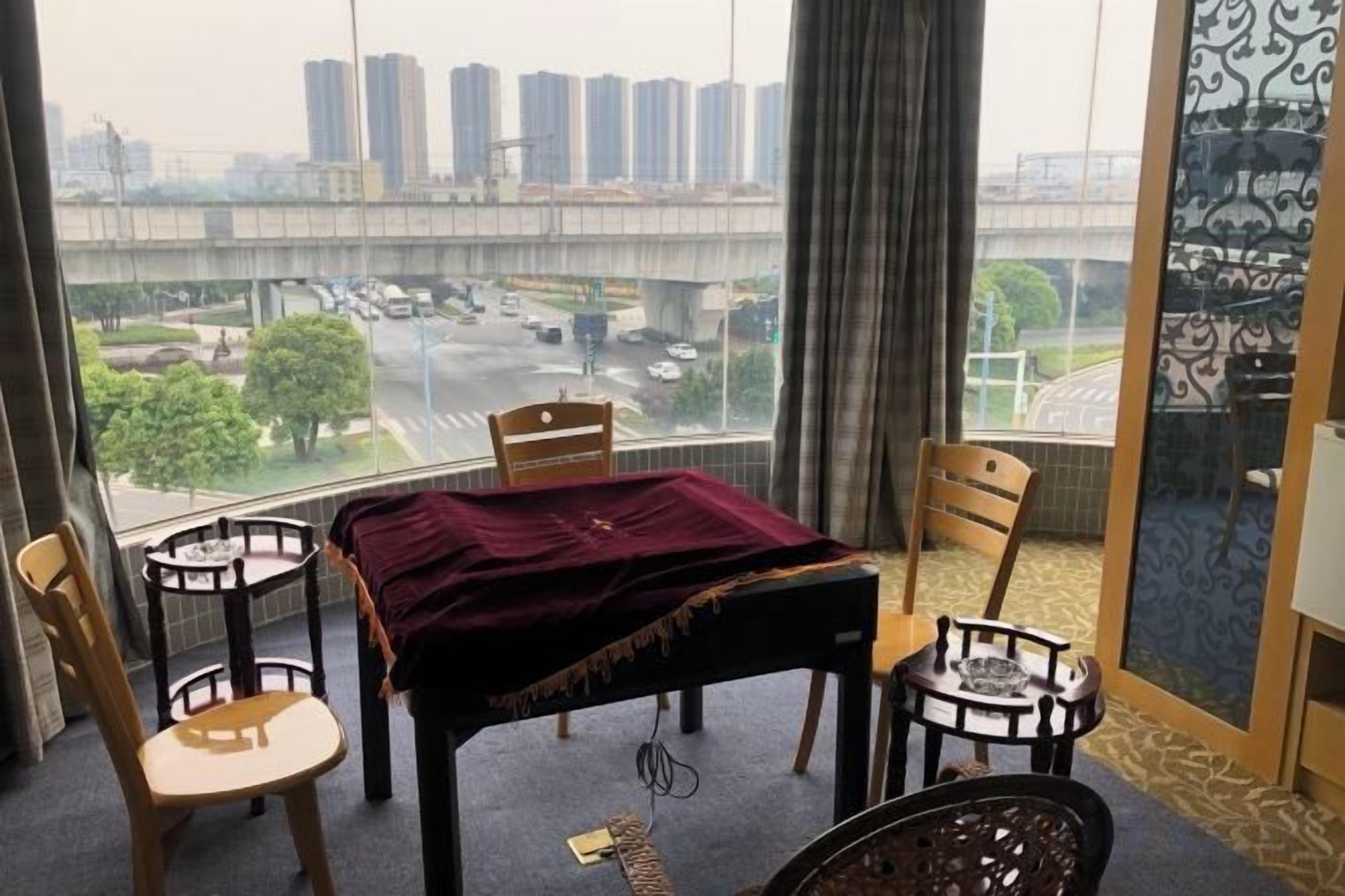 Una habitación con una mesa y sillas, vista de un paisaje urbano a través de un ventanal grande y una cortina estampada.