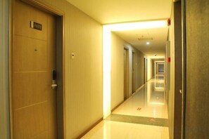 Pasillo de hotel con puertas, suelo de baldosas e iluminación empotrada en el techo.