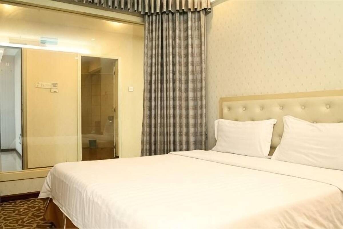 A hotel room with a large bed, a glass door leading to a bathroom, and a curtain.