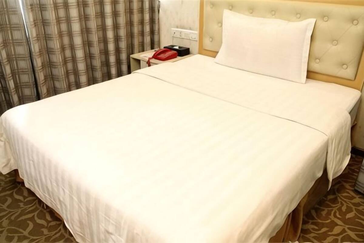 A hotel room with a large bed, a headboard, a bedside table with a red object, and a patterned carpet.