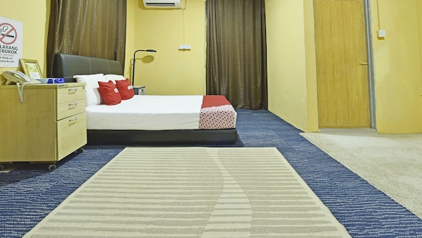 A hotel room with a bed, a desk, a lamp, curtains, an air conditioning unit, and a door. - OYO 90535 Wakaf Bharu Inn (Tumpat)