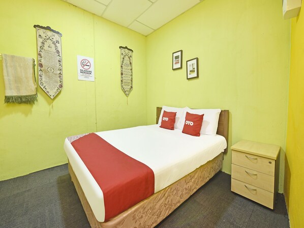 A hotel room with a bed, a nightstand, and a wall with religious decorations and a no-smoking sign. - OYO 90535 Wakaf Bharu Inn (Tumpat)