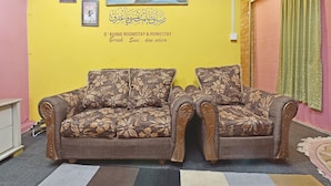 A room with two brown floral sofas, a yellow wall with a painting and Arabic script, and a green curtain. - OYO 90535 Wakaf Bharu Inn (Tumpat)