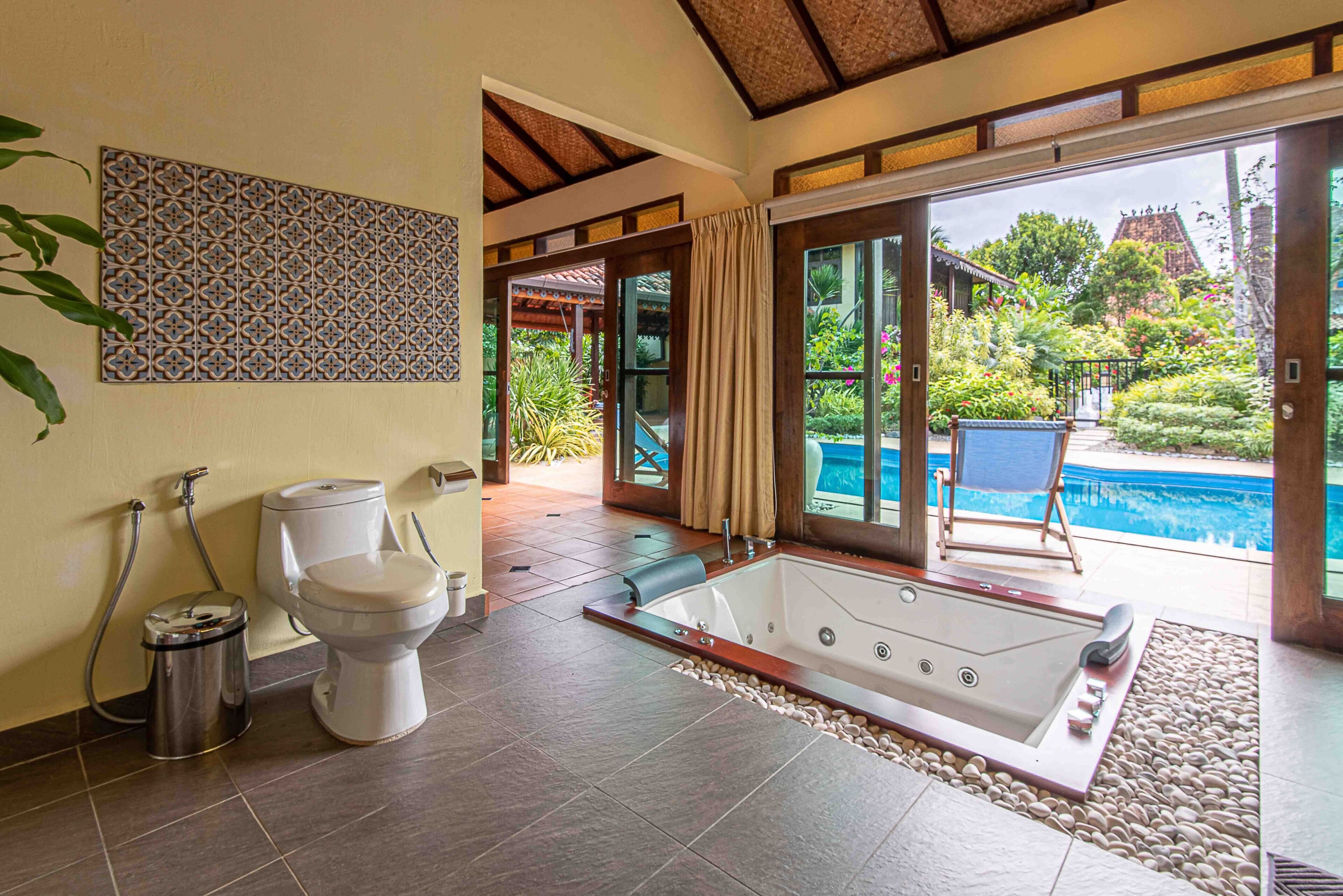 Un baño con bañera, inodoro y ducha, que ofrece vistas a una piscina y jardín.