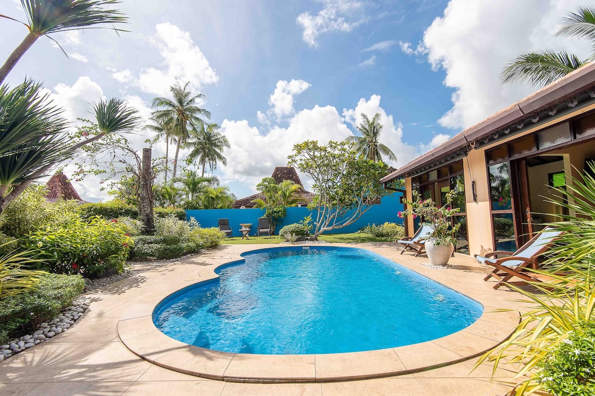 Ein Pool mit geschwungener Kante, umgeben von Palmen und einer blauen Wand.