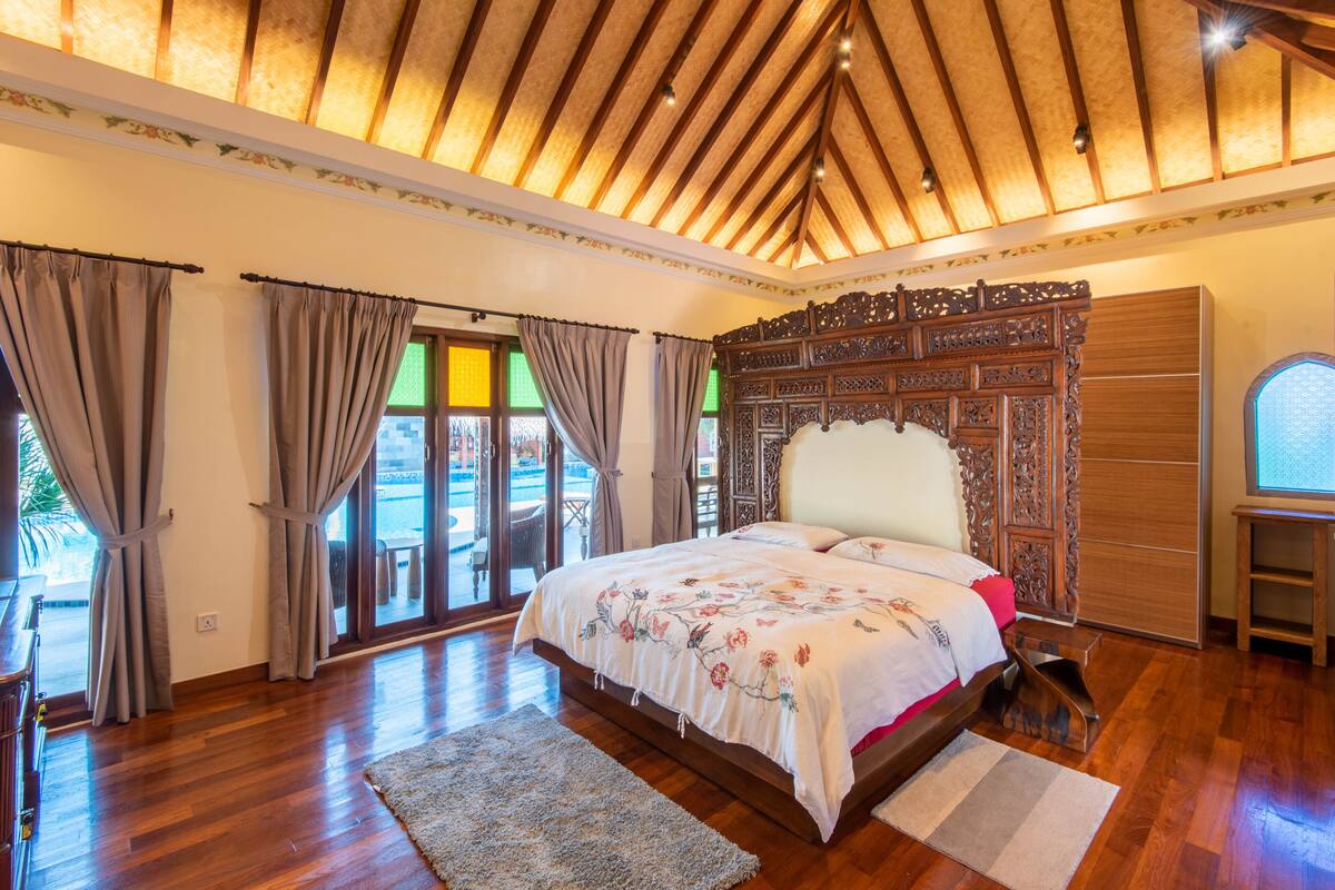Ein geräumiges Schlafzimmer mit einem großen Bett, Holzboden und Blick durch die Glastüren.