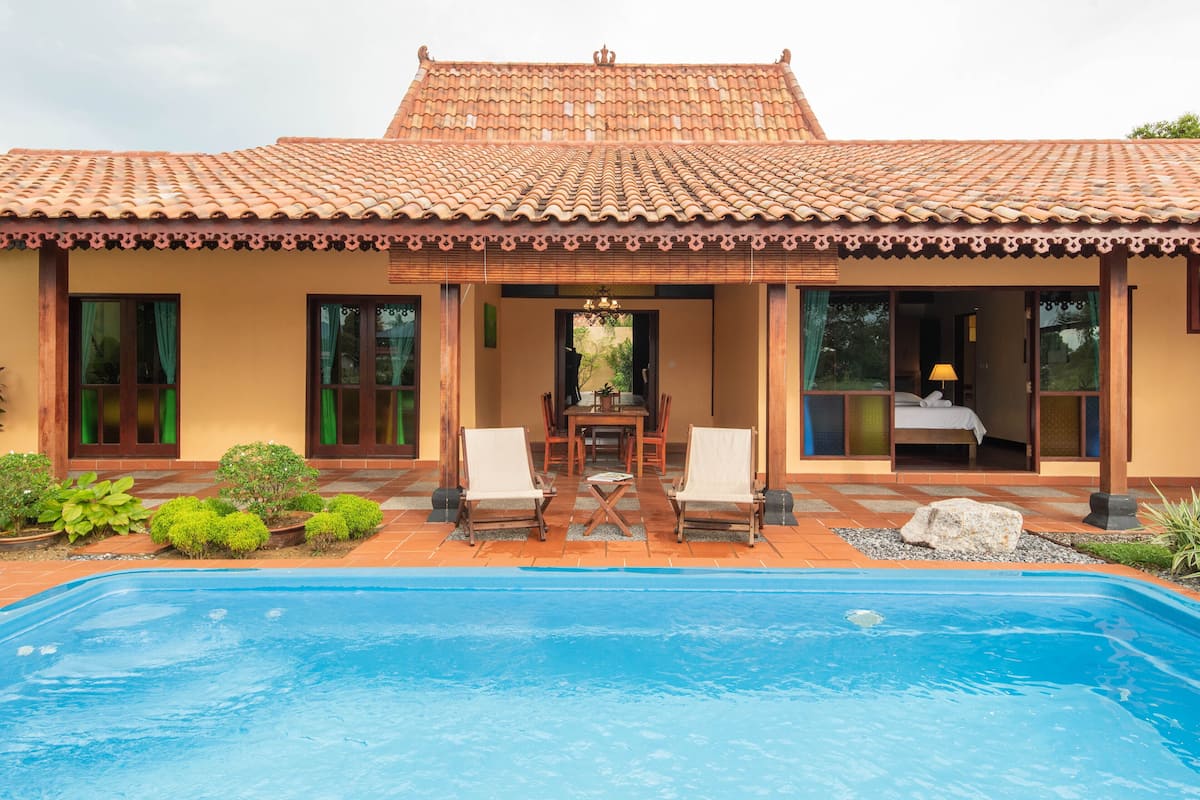 Ein traditionelles Haus mit Ziegeldach, einem Pool und einer Terrasse mit Stühlen und Tisch.