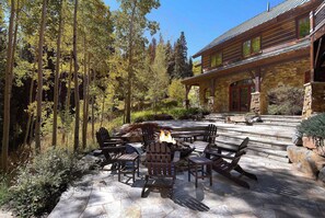 Un patio de piedra con sillas Adirondack, una fogata y una chimenea de piedra.