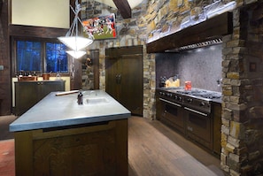 Una cocina con pared de piedra, una isla grande con pileta y estufa.