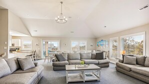 A spacious living room with a sectional sofa, a coffee table, and a dining area with a table and chairs. - 1486 - Blue Retreat - Whalehead Corolla Escape w/ Pool & Hot Tub (Corolla)