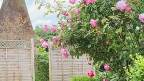 A garden with blooming pink roses, a brick wall, and a wooden fence. - Oast Cottage (Maidstone)