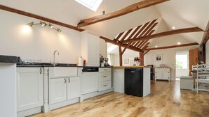 A spacious kitchen with wooden beams, white cabinetry, and a dishwasher. - Oast Cottage (Maidstone)