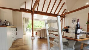 A spacious kitchen with wooden flooring, a dining table with chairs, and a wine bottle on the table. - Oast Cottage (Maidstone)