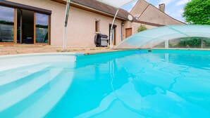 Une piscine entourée de parois en verre, un barbecue et une maison dotée d’une porte-fenêtre coulissante.