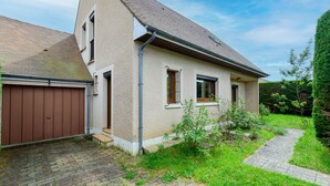 Une maison à deux étages avec un toit en pente, un garage et un petit jardin agrémenté d’un chemin menant à l’entrée.