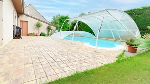 Une piscine entourée d’une enceinte en verre, bordée d’une terrasse pavée et d’une pelouse.