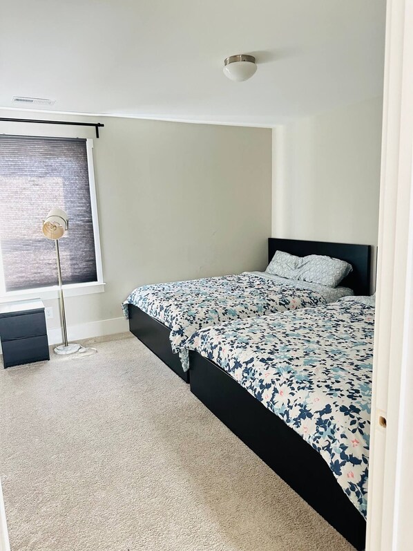 Une chambre à coucher avec un lit, une lampe sur pied, une fenêtre avec des stores et un luminaire au plafond.