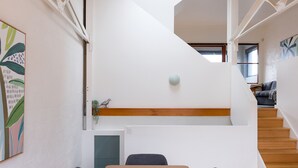 Ein modernes Interieur mit einer Treppe, einem Essbereich mit Tisch und Stühlen und einer kleinen Pflanze auf einem Regal.