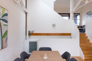 A modern interior with a staircase, a dining area with a table and chairs, and a small plant on a shelf. - Just My Type Richmond Retreat with Parking (Richmond)