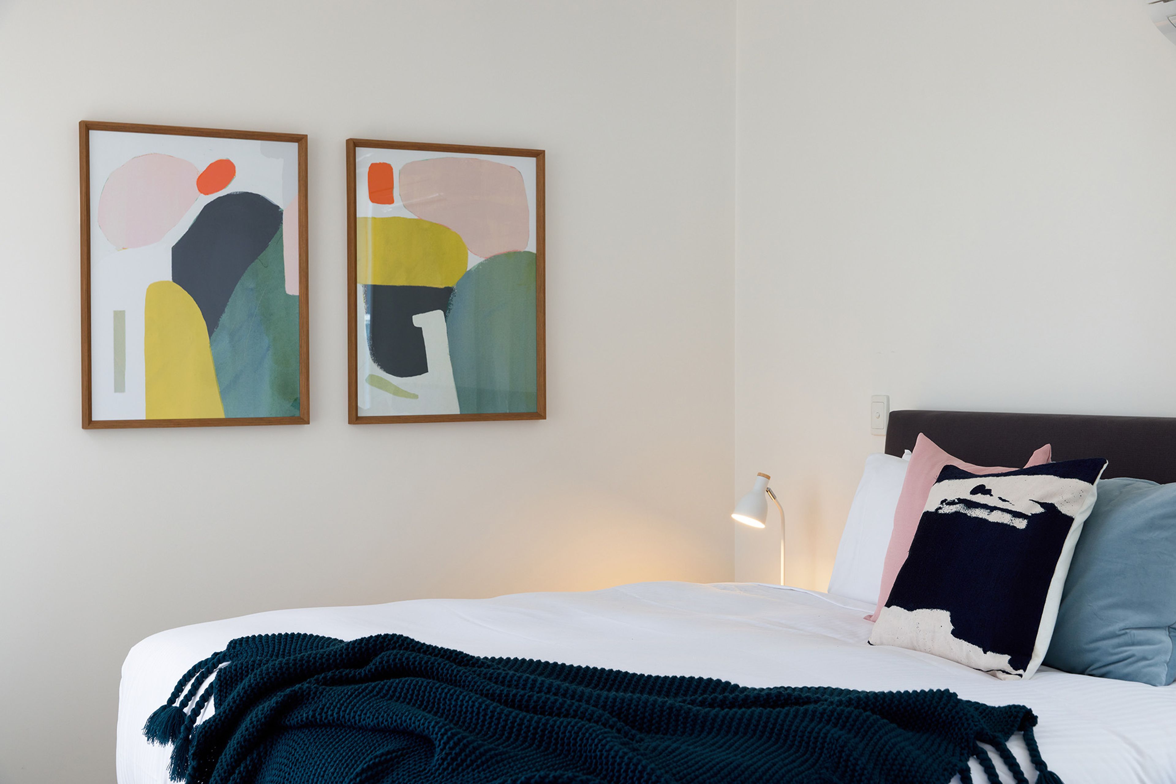 Ein Schlafzimmer mit einem Bett, Kissen, einer Decke und zwei abstrakten Bildern an der Wand.