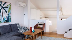 Ein modernes Wohnzimmer mit einem grauen Sofa, einem Holztisch und einem farbenfrohen abstrakten Gemälde an der Wand.