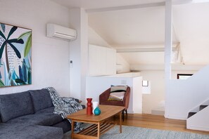 A modern living room with a grey sofa, a wooden coffee table, and a colorful abstract painting on the wall. - Just My Type Richmond Retreat with Parking (Richmond)