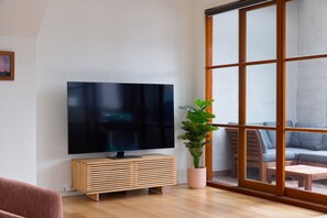 Een moderne woonkamer met een flatscreen televisie bevestigd aan een houten console, een potplant en een grote schuifglazen deur die leidt naar een buiten zitgedeelte.