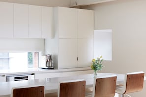 A modern kitchen with white cabinets, a coffee machine, and a vase with flowers on the counter. - Just My Type Richmond Retreat with Parking (Richmond)