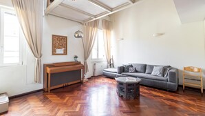 Uma sala de estar ampla com piso de madeira em padrão herringbone, um sofá cinza, uma mesa de centro de madeira e um radiador.