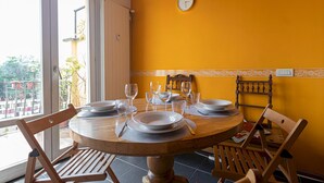 Mesa posta com pratos, copos e talheres em um quarto com paredes amarelas e vista através de uma porta de vidro.
