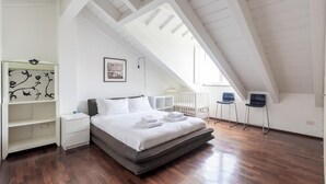 Quarto moderno com teto estilo loft, cama com roupa de cama branca, guarda-roupa branco e berço.