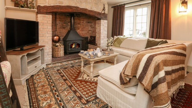 Una sala de estar acogedora con chimenea de piedra, televisor, sofá y alfombra estampada.