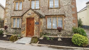 Una casa de piedra con puerta de madera, número 51, y un pequeño jardín delantero con una planta en maceta y una roca.