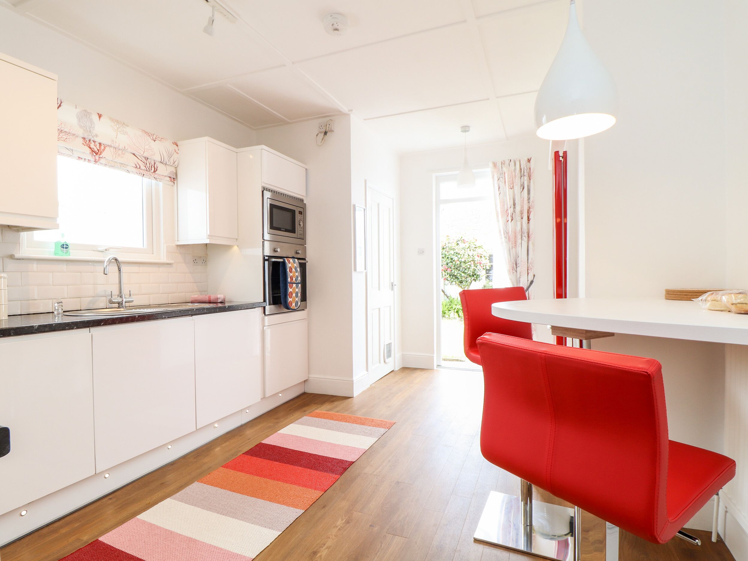 A modern kitchen with white cabinets, a microwave, oven, and a red chair at a dining table.