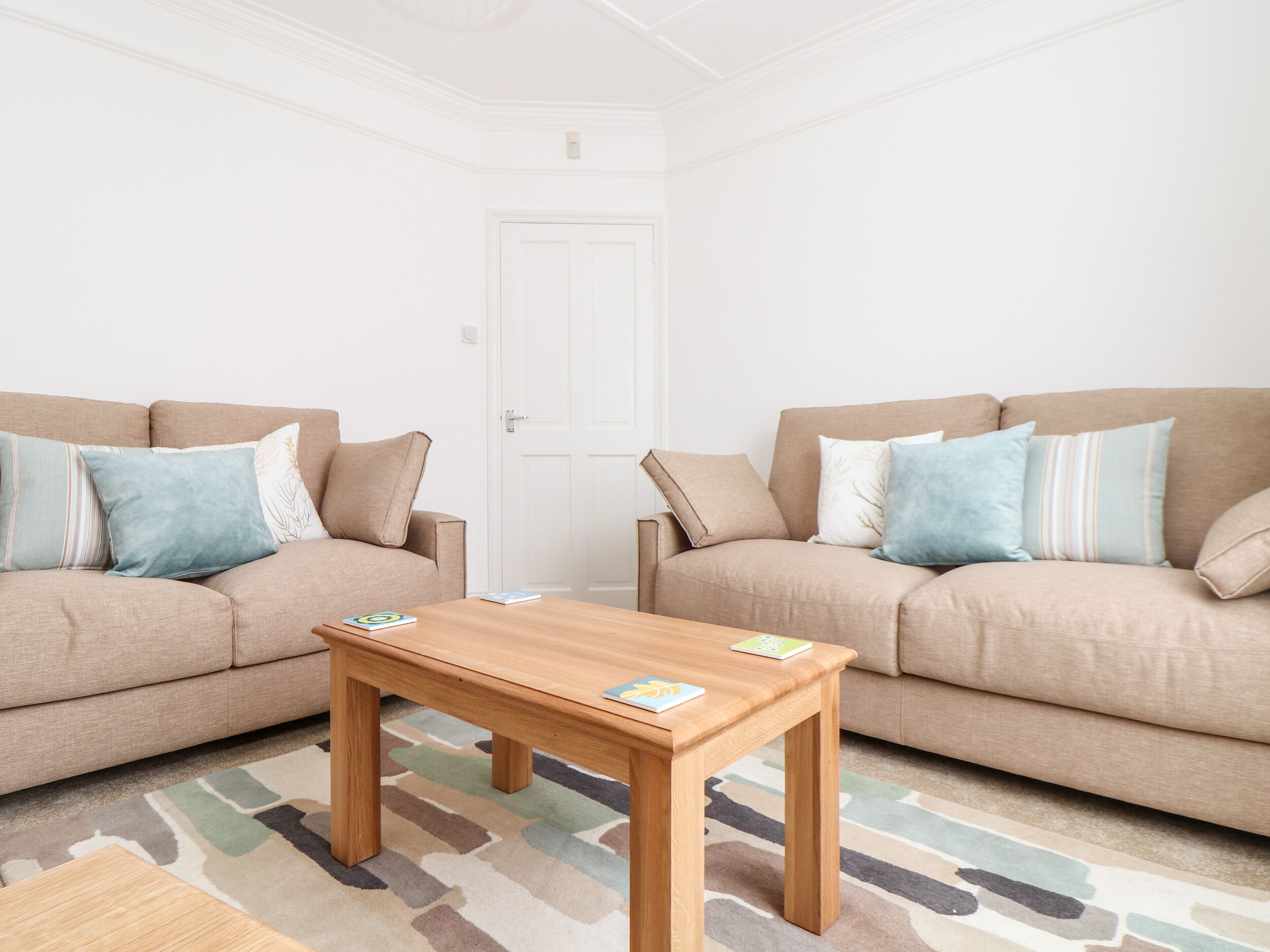 A living room with two beige sofas, a wooden coffee table, and a patterned rug.
