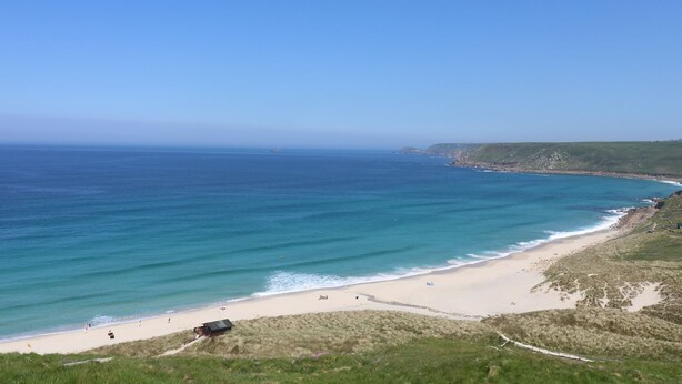 A coastal landscape with a beach, grassy dunes, and a clear blue sky.