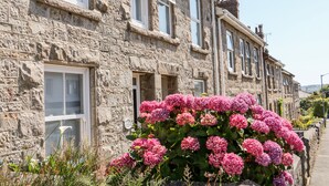 A stone building with multiple windows and a large bush of pink flowers in front.