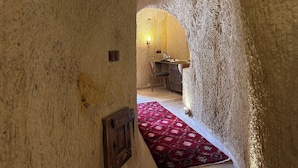 Un estrecho pasaje con paredes texturizadas que conduce a una habitación con una mesa de madera, sillas y una alfombra roja estampada.