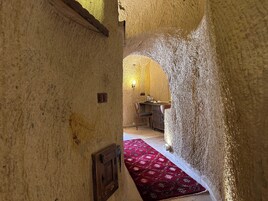 Un estrecho pasaje con paredes texturizadas que conduce a una habitación con una mesa de madera, sillas y una alfombra roja estampada.