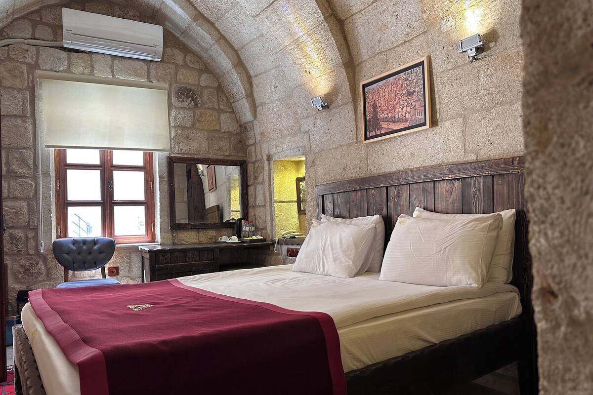 A stone-walled bedroom with a bed, a wooden headboard, a mirror, and a framed picture on the wall.