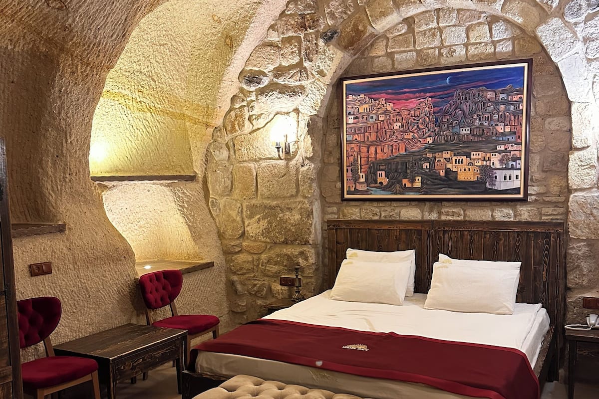 A stone-walled bedroom with a bed, a red upholstered chair, a bench, and a bathtub.