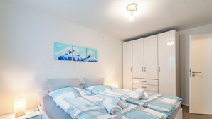 Una cama bien tendida con una colcha estampada, una lámpara de noche y un cuadro colgado en la pared.